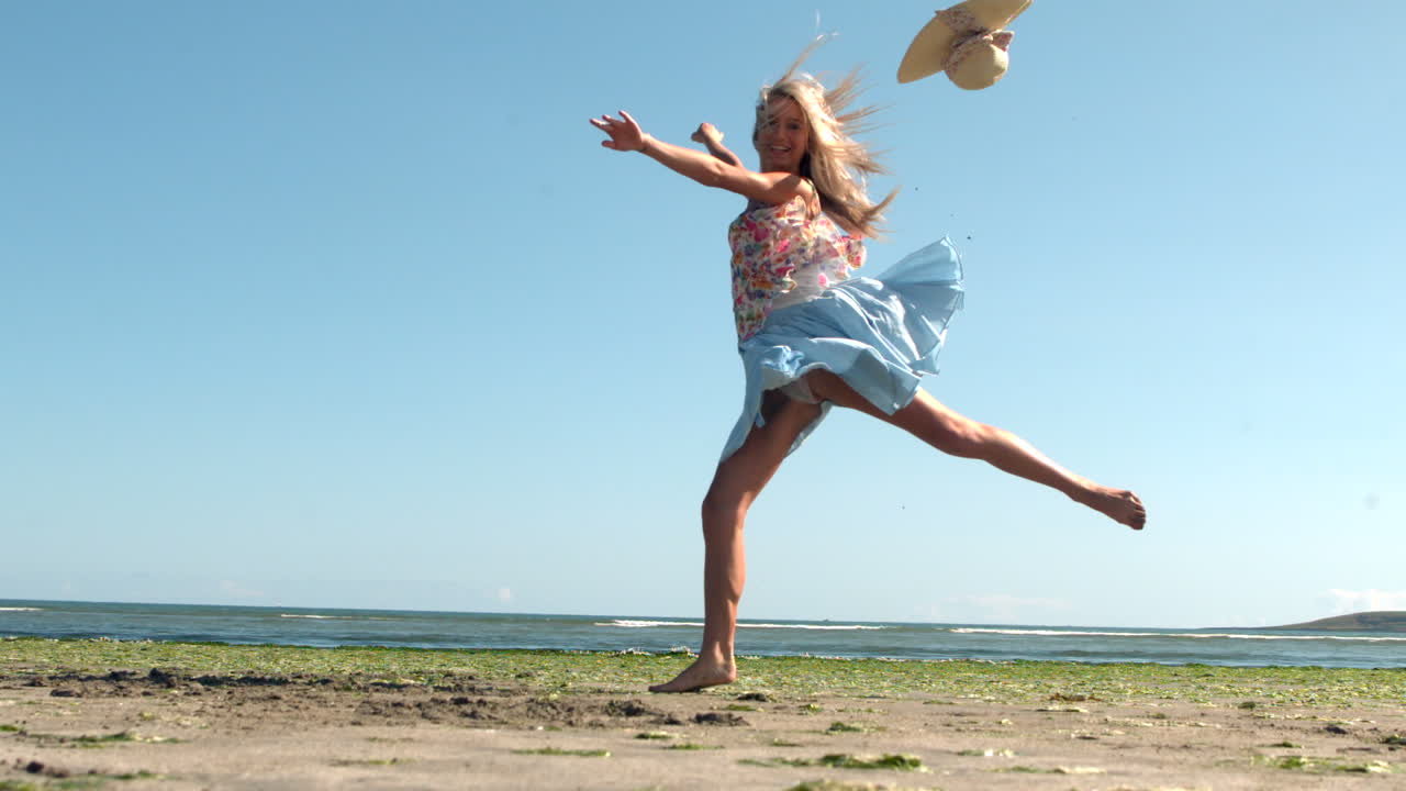 Bionda attraente che esegue un salto di balletto sulla spiaggia