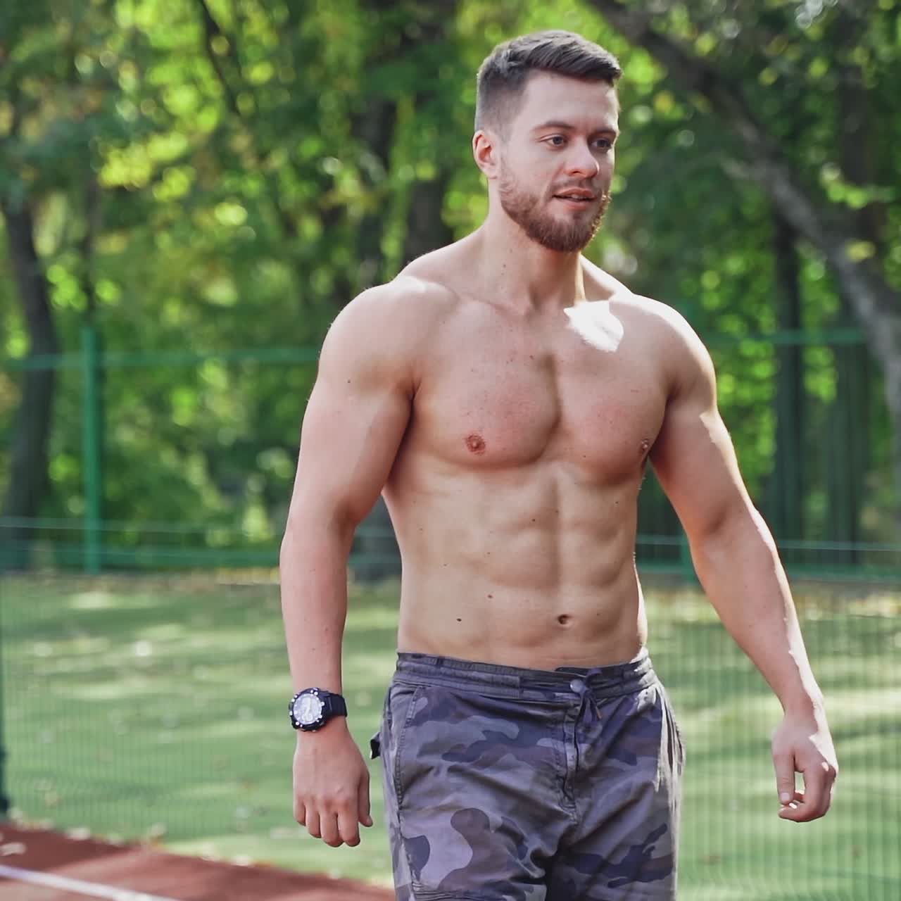 Muscular runner on the outdoor stadium. Portrait of a strong athlete without shirt prepares for running on a track. Slow motion.