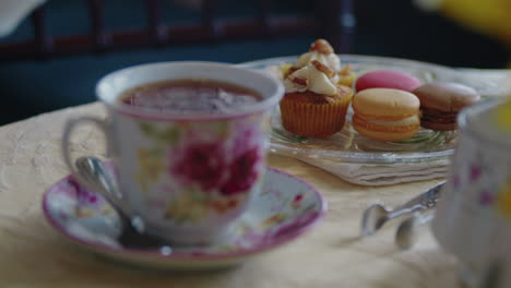 enfoque del estante de una taza de té a un plato de pasteles elegantes y macrones franceses