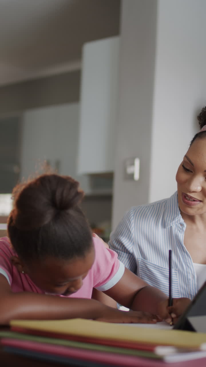 Vertical video of biracial mother and daughter using tablet and doing homework, slow motion