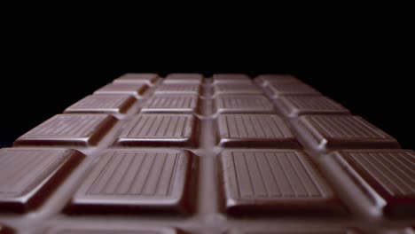 macro shot of long sweet milk chocolate bar isolated on black background