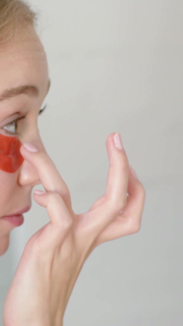 Vertical video: Prompted by red under-eye patch woman adjusting with right hand at vanity, securing