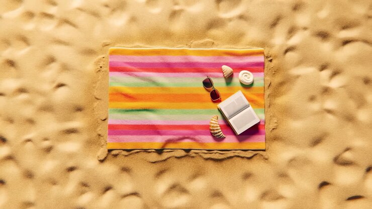 Telo mare a righe colorate con libro e occhiali da sole sulla sabbia