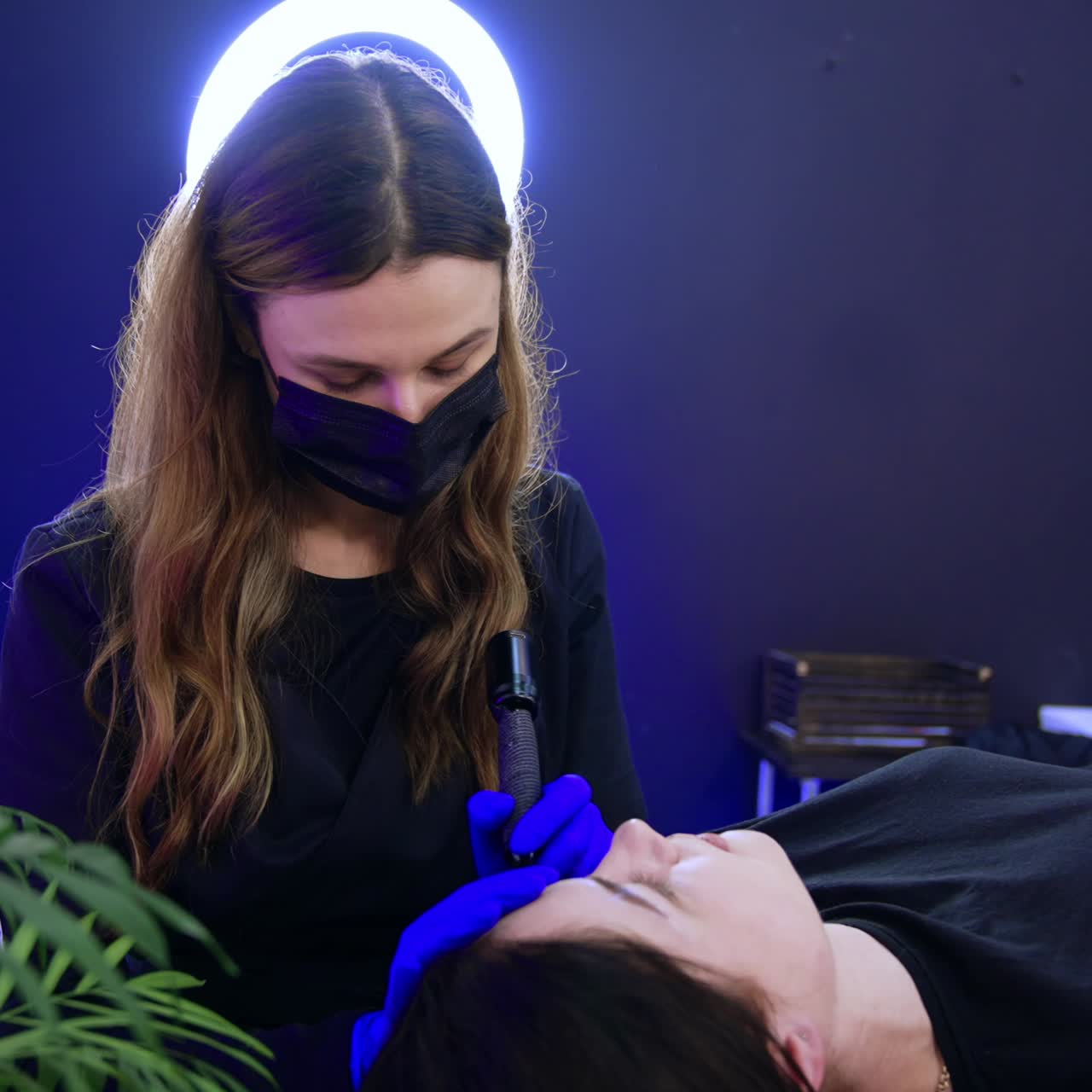 Long-haired brow-master in mask performs the procedure for the client. Beauty salon eyebrow make up for a female client