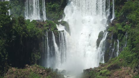 Dramatic-Rough-Waterfall-in-Mossy-Green-Rainforest-Landscape,-Aggressive-Waterfalls-Crashing-onto-Emerging-Large-Rocks-in-Iguacu-Falls,-Lots-of-Waterfall-Splashback-in-Brazil,-South-America