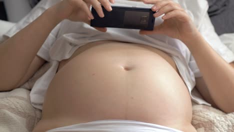 mujer embarazada con el vientre desnudo descansando en casa y usando el teléfono móvil