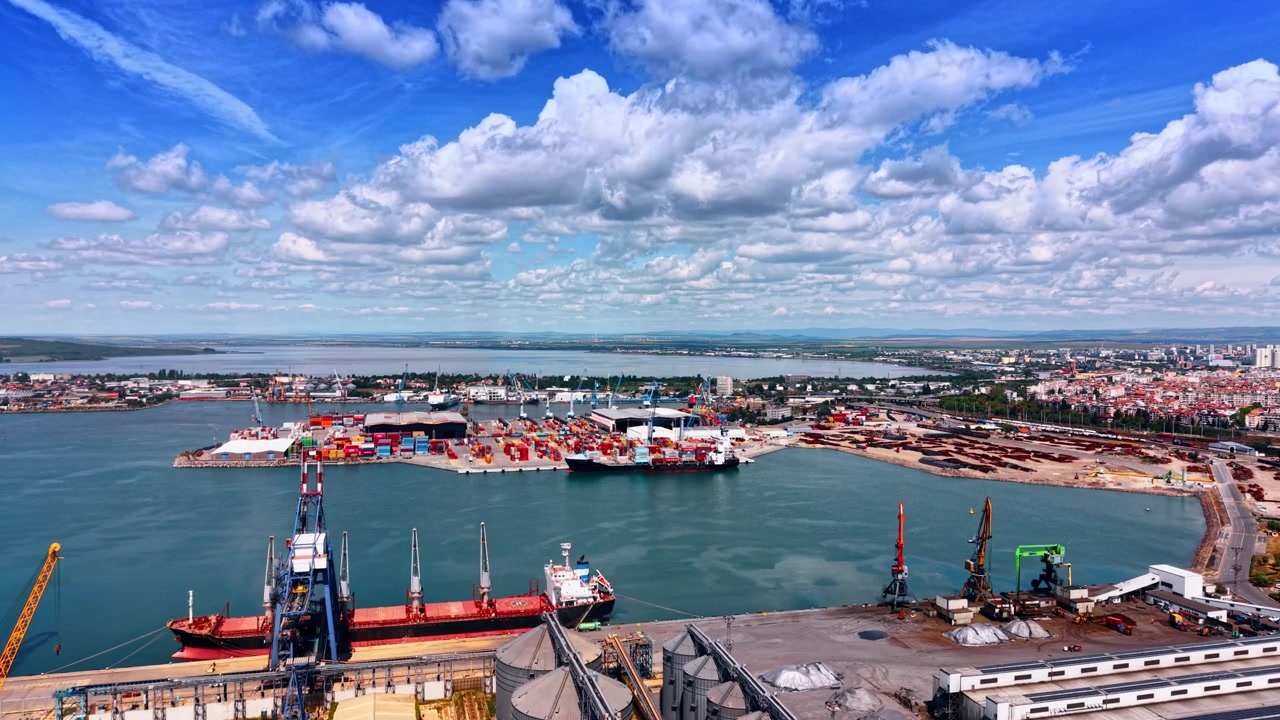 Burgas, Bulgaria, 10 aprile 2026: Veduta dall'alto di silos per cereali e di una nave portarinfuse in banchina. Ripresa aerea di serbatoi di stoccaggio cilindrici, gru portuali e una nave rossa con area container sullo sfondo.