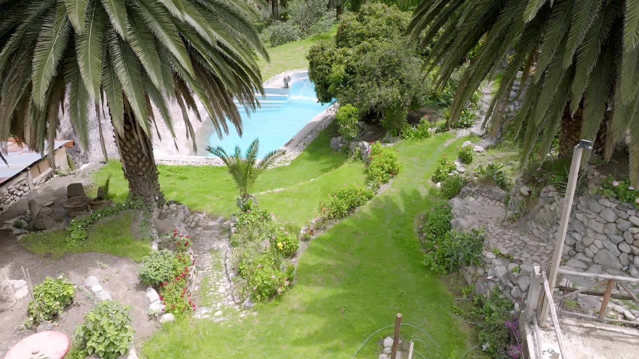 Drone shot descending over the Oasis of Sangalle, revealing the palm trees surrounding the oasis and the stunning themed pool, set against the breathtaking landscape of the Colca Canyon.