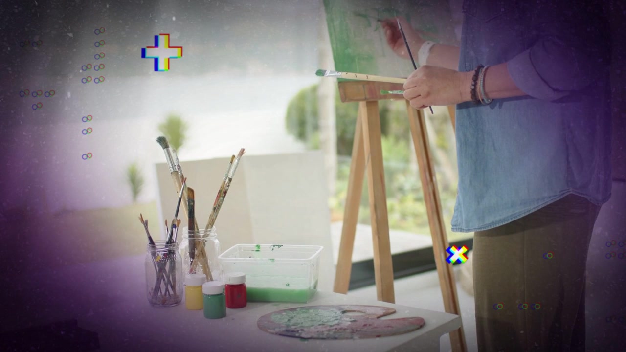筆を手に取り、絵の具を混ぜ、緑色のストロークでアートを制作するアーティスト。端には紫色のオーバーレイ。
