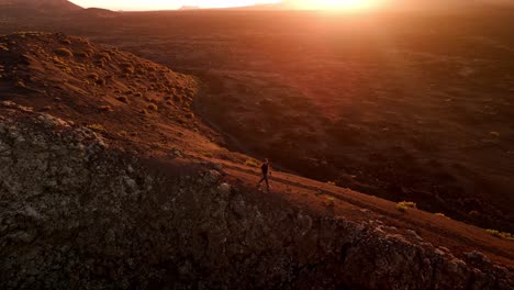 a stunning aerial drone shot capturing a solitary man walking along the rim of volcano del cuervo at sunset in lanzarote, canary islands, spain.