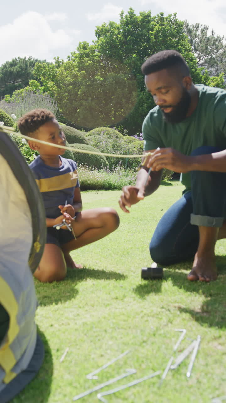 Vídeo vertical de pai e filho afro-americanos montando barraca, em câmera lenta