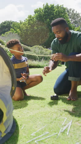 vertical video of african american father and son pitching tent, in slow motion