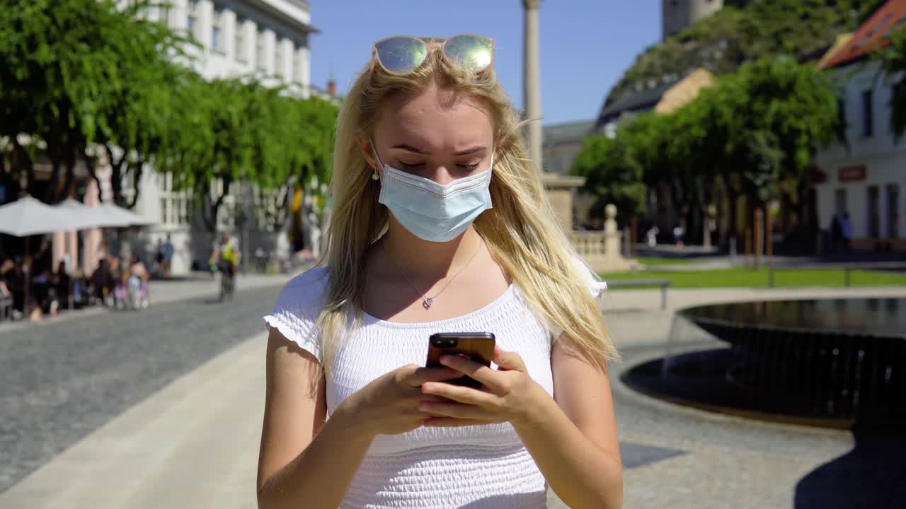 covid-19 молодая красивая блондинка женщина-подросток проверяет телефон на общественной городской площади