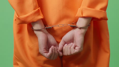 close up of male prisoner's hands in handcuffs while he is standing on the green screen background