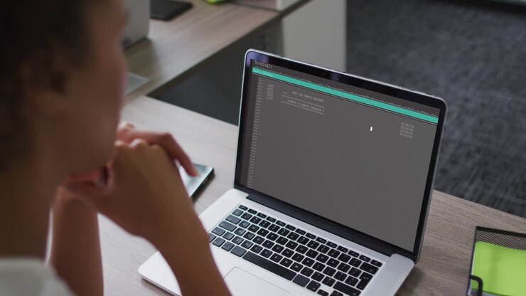 Biracial woman sitting at desk watching coding data processing on laptop screen
