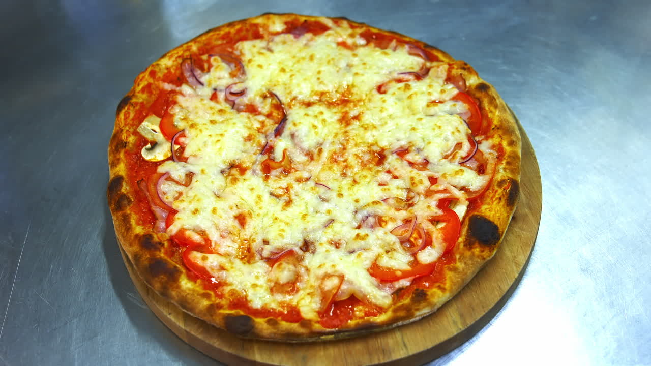 Hot yummy pizza with much cheese, bacon, tomatoes on top. Chef puts freshly prepared piza on wooden board.