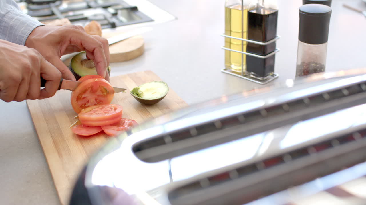 Slicing tomatoes and avocado on cutting board, person preparing fresh ingredients