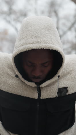 primer plano de un joven con una sudadera con capucha cálida enfocándose durante un ejercicio de flexiones en un entorno al aire libre nevado, su capucha está levantada, y su postura refleja concentración y determinación mientras entrena en clima frío