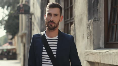 Portrait-Of-A-Handsome-Young-Man-In-Stylish-Outfit-Taking-Off-Glasses-And-Smiling-At-The-Camera-In-An-Old-Town-Street