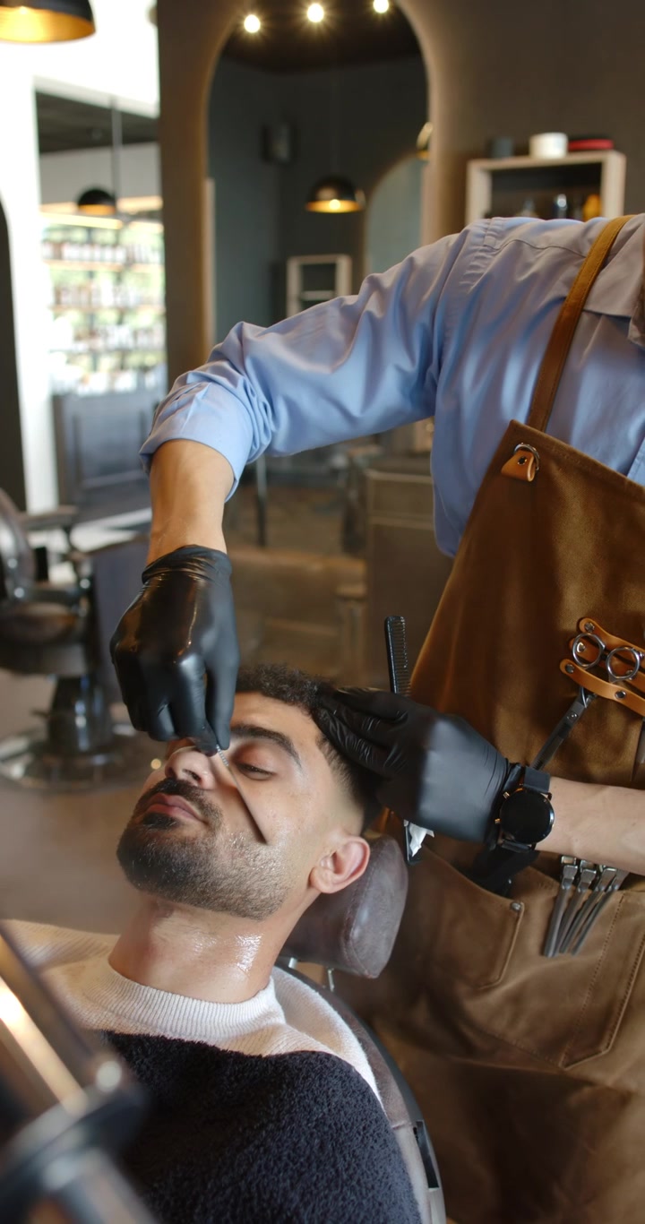 Vertikal video: Afrikansk barber forstøver, former øjenbryn og hårgrænse med skraber i salonen