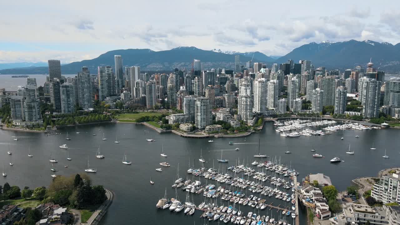 Panorama drone shot of Vancouver City with high-rise buildings and mountain range in background during cloudy day - marina port with boats and sailing boats in foreground a falls Creek river