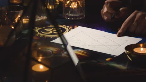 primer plano de una mujer dando una lectura de la astrología lagna o gráfico de nacimiento en la mesa a la luz de las velas 1