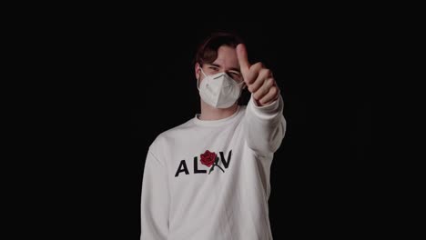 trendy young man unsure thumb gesture wearing mask, wide, black background