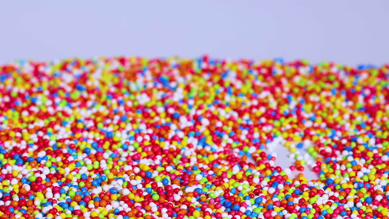 A dense layer of colorful sprinkles spreads evenly across a flat surface, creating a lively and textured pattern.