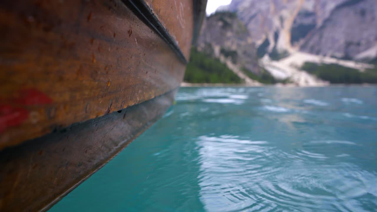 toma creativa de primer plano del exterior de un bote de remos de madera deslizándose a través del agua de un lago de montaña azul, el lago di braies en italia
