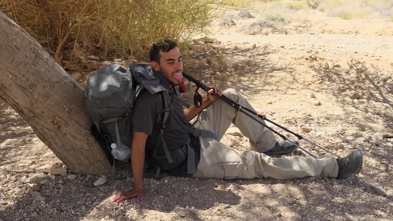 En utmattet turgåer hviler i skyggen av et tre i Makhtesh Ramon-krateret, Negev-ørkenen, Sør-Israel