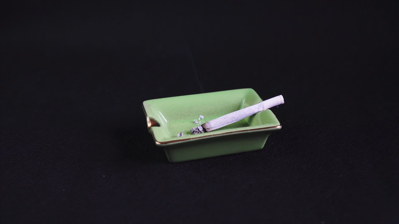 Rolled Cigarette or Joint burning out, legalised marijuana on green Ashtray