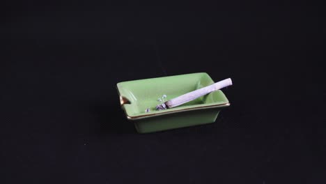 rolled cigarette or joint burning out, legalised marijuana on green ashtray