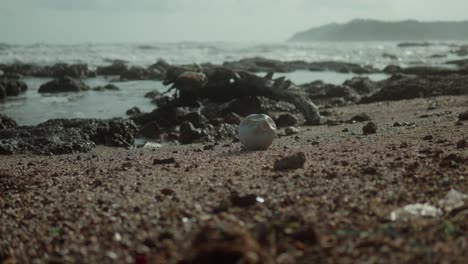 Ein-Vermüllter-Strand-Mit-Einer-Aluminiumdose-Im-Fokus-Und-Dem-Meer-Im-Hintergrund