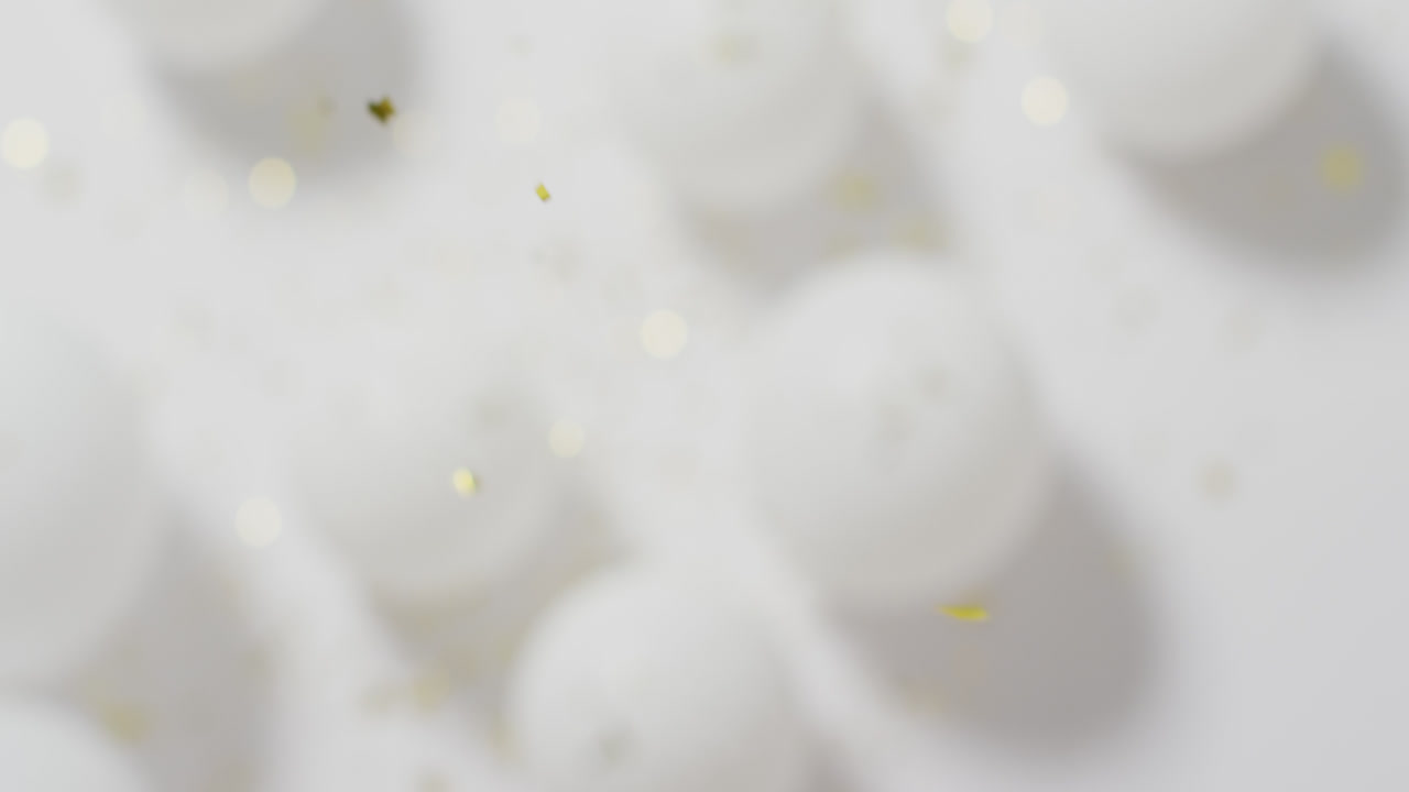 Video of gold confetti falling over defocussed white balloons on white background
