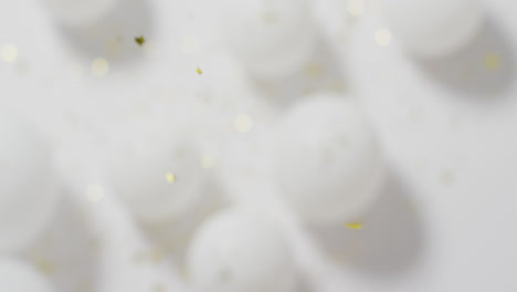 video of gold confetti falling over defocussed white balloons on white background