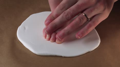 mother carefully push newborn baby foot to create footprint on white clay