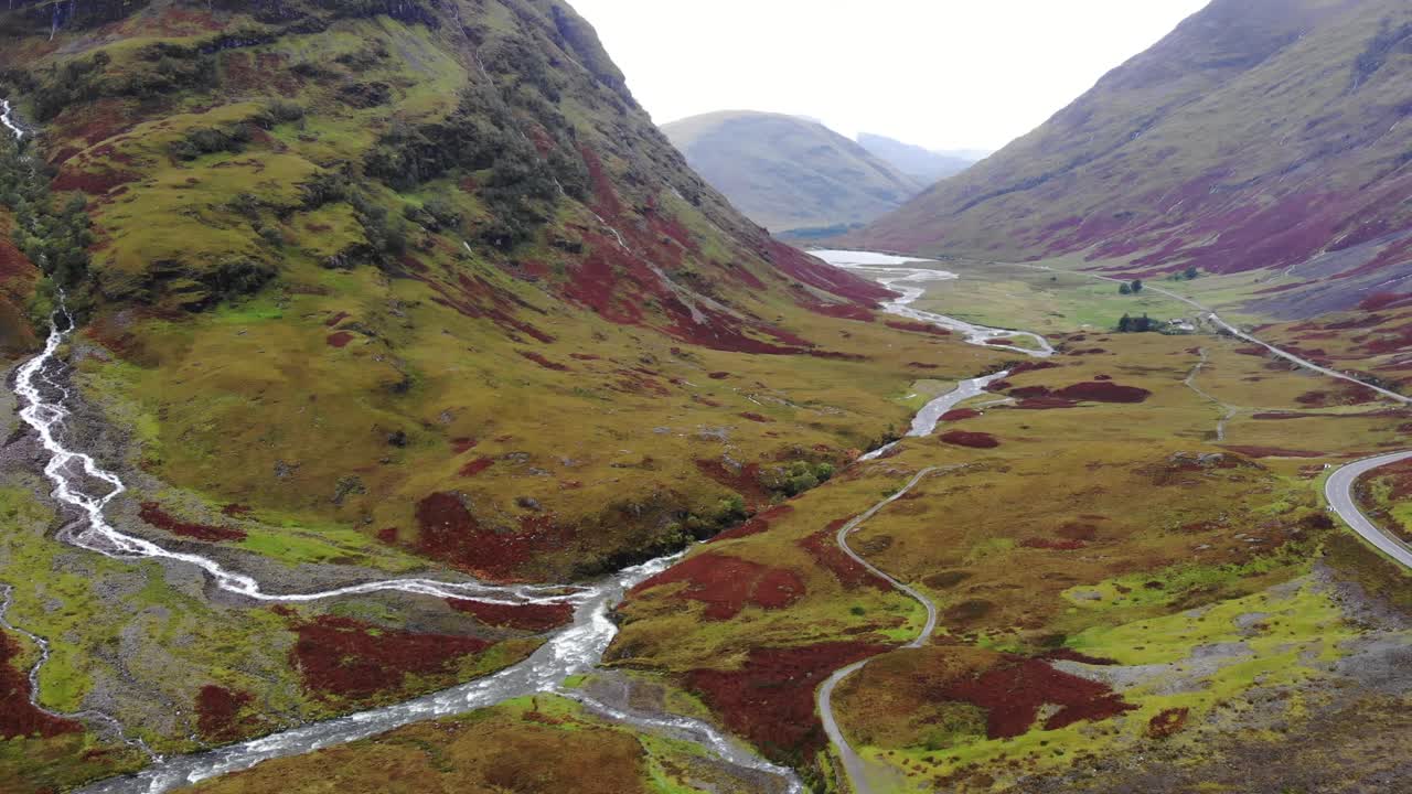 Espectacular toma aérea con paneo a la derecha del valle de las montañas de Glencoe, mostrando ríos fluyendo y resaltando la gama de colores.