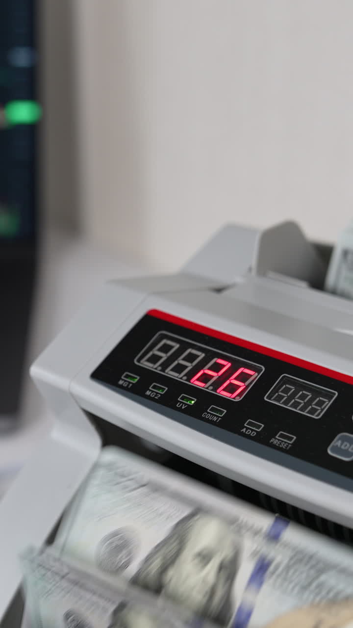 Equipment for counting cash. Male hand puts a wad of dollars into money counting machine. Close up. Blurred backdrop. Vertical video