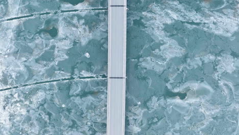 aerial view above cars driving on a bridge at a frozen lake, winter day in iceland - top down, drone shot