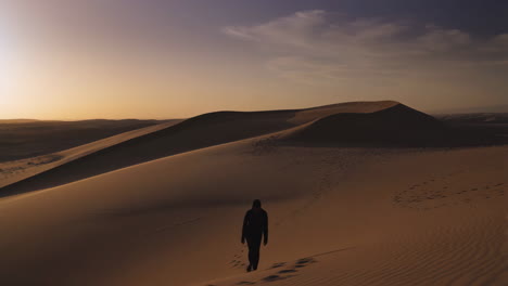 Solitary Figure Walking on Desert Sand Dunes at Sunset