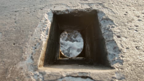 blue sea water foaming up violently, rising up through cement tube hole in slowmo