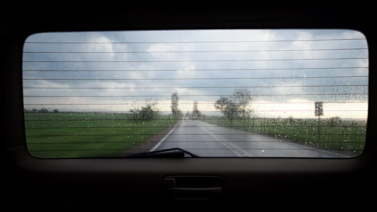 A journey unfolds as rain falls on the road while a bus passes by. Dark clouds loom overhead, highlighting the vibrant greenery that surrounds the highway