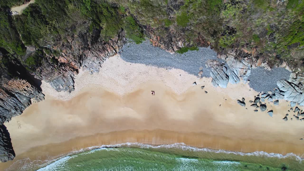 video de dron de 4k volando hacia arriba y lejos de una pareja que está acostada en una playa de arena blanca rodeada de exuberantes acantilados verdes con olas turquesas del océano rodando, parque nacional noosa, queensland, australia