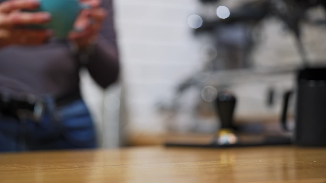 Hot drink in hands. Woman waiter putting a coffee cup with hands on table. Serving a hot drink in blue cup on blur background. Close-up.