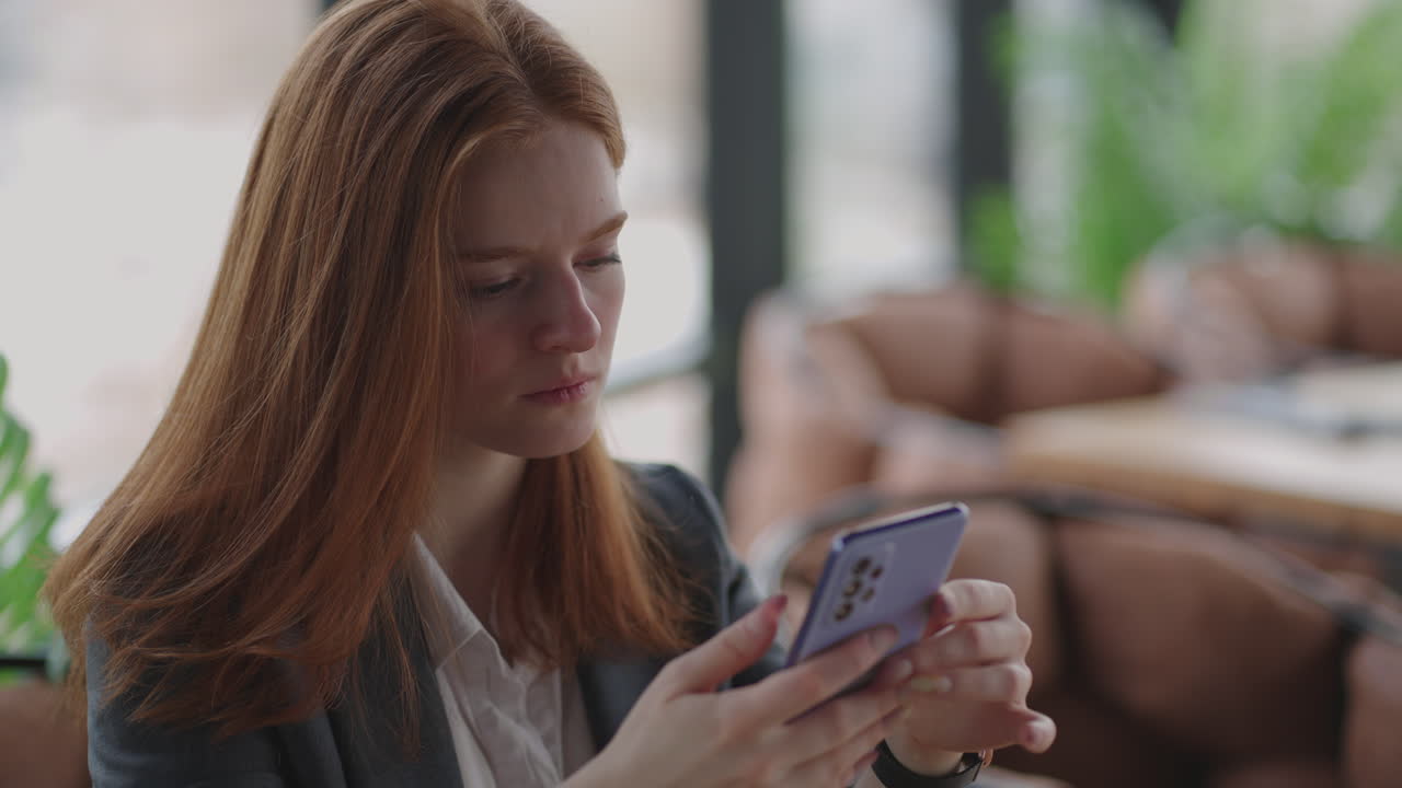 Beautiful young business woman using phone in office. Woman using a smartphone and leaning on a window texting sending emails planning meetings networking online browsing messages on mobile phone