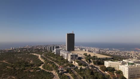 vuelo de drones de un edificio alto en las afueras de una ciudad con un parque y senderos naturales, haifa, israel