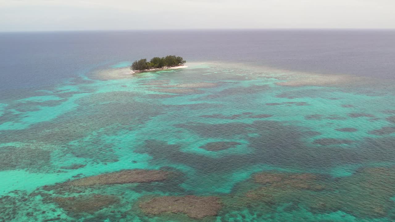 imágenes aéreas de una hermosa isla pequeña de arrecifes de coral rodeada de arena y un océano azul profundo que se extiende hasta el horizonte
