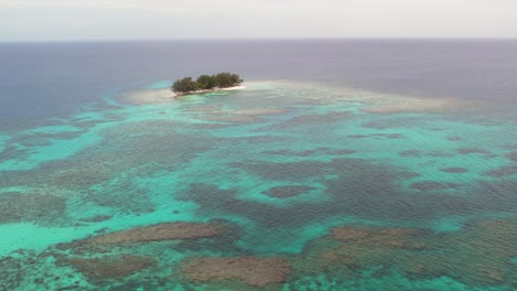 Imágenes-Aéreas-De-Una-Hermosa-Isla-Pequeña-De-Arrecifes-De-Coral-Rodeada-De-Arena-Y-Un-Océano-Azul-Profundo-Que-Se-Extiende-Hasta-El-Horizonte