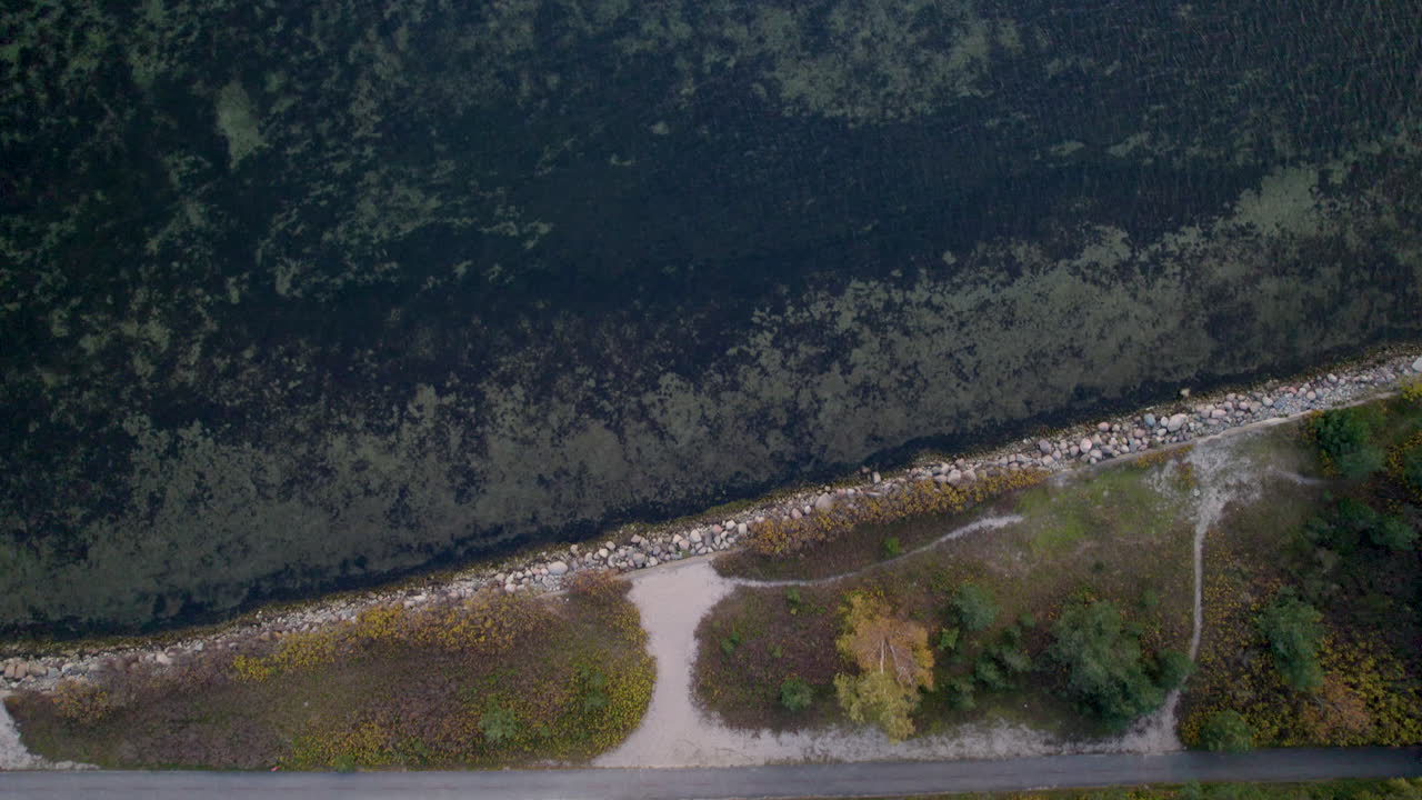 Aerial view of a meandering dirt path next to a rocky creek, surrounded by autumnal forest