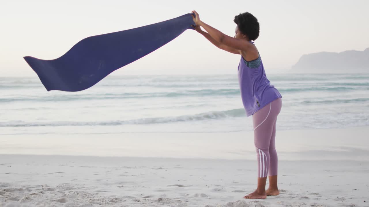 mujer afroamericana con colchoneta de yoga en una playa soleada